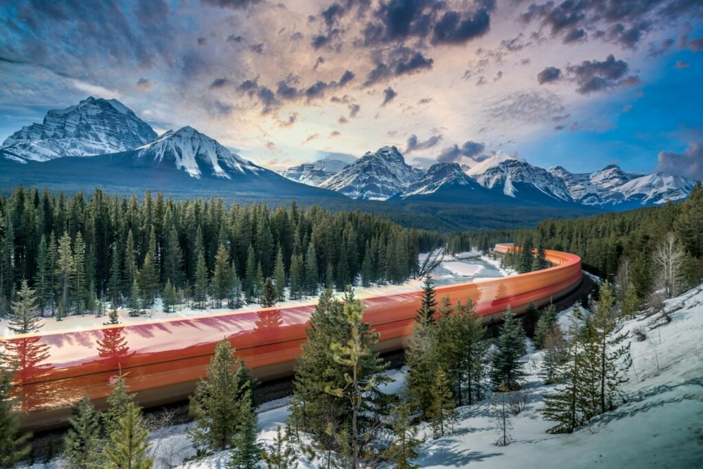 A red train speeds through a snowy forest with majestic mountains in the background.