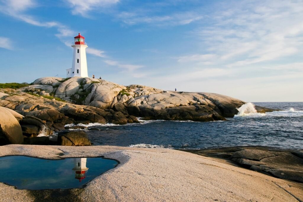 Lighthouse on rocky coast with ocean waves and bright sky, perfect for maritime themes.