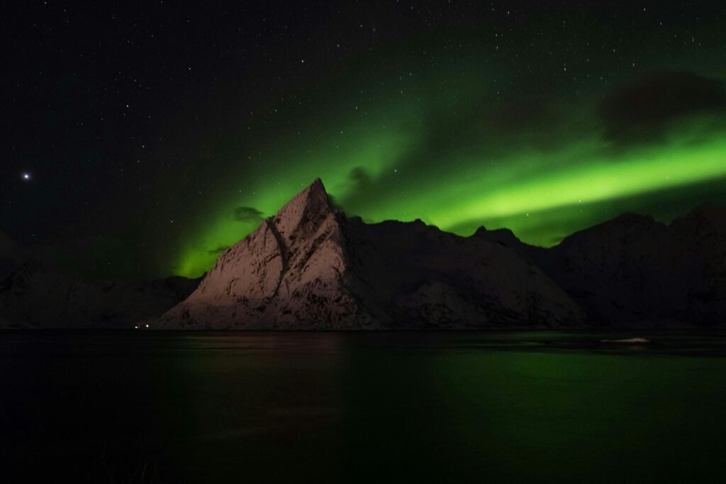 Breathtaking view of the Northern Lights over a snow-capped mountain in the Arctic night.