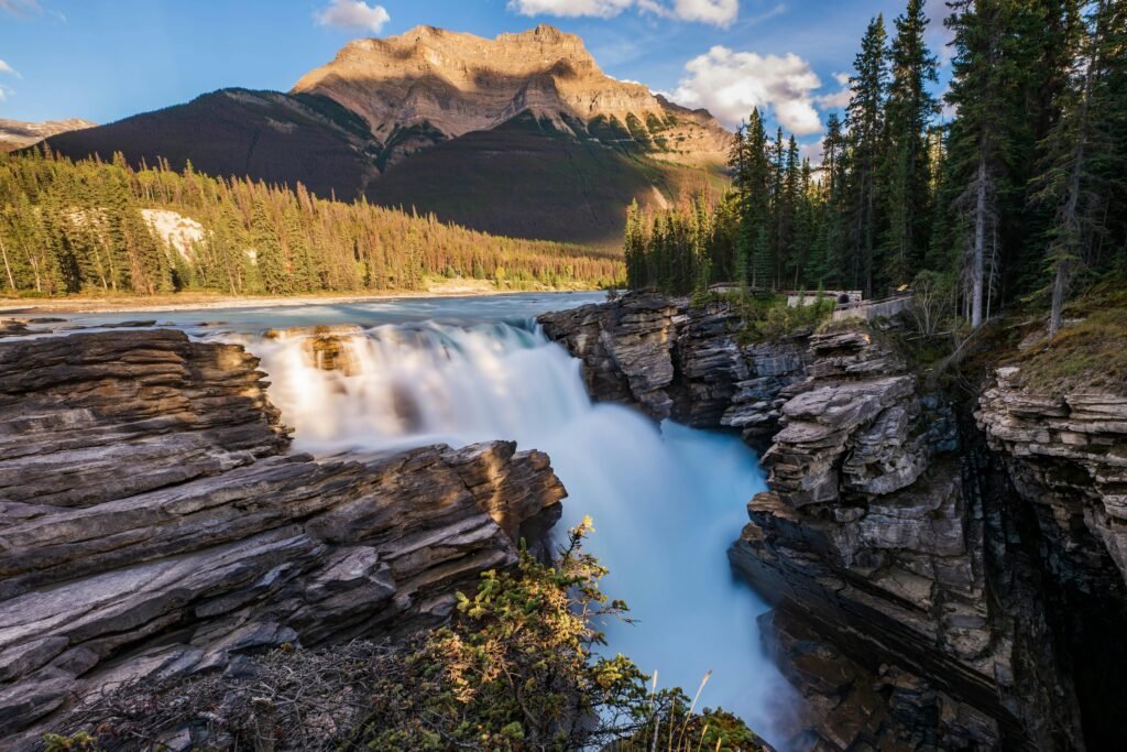 Scenic view of Athabasca Falls with rugged rocks and evergreen forests in Jasper National Park, Alberta, Canada.