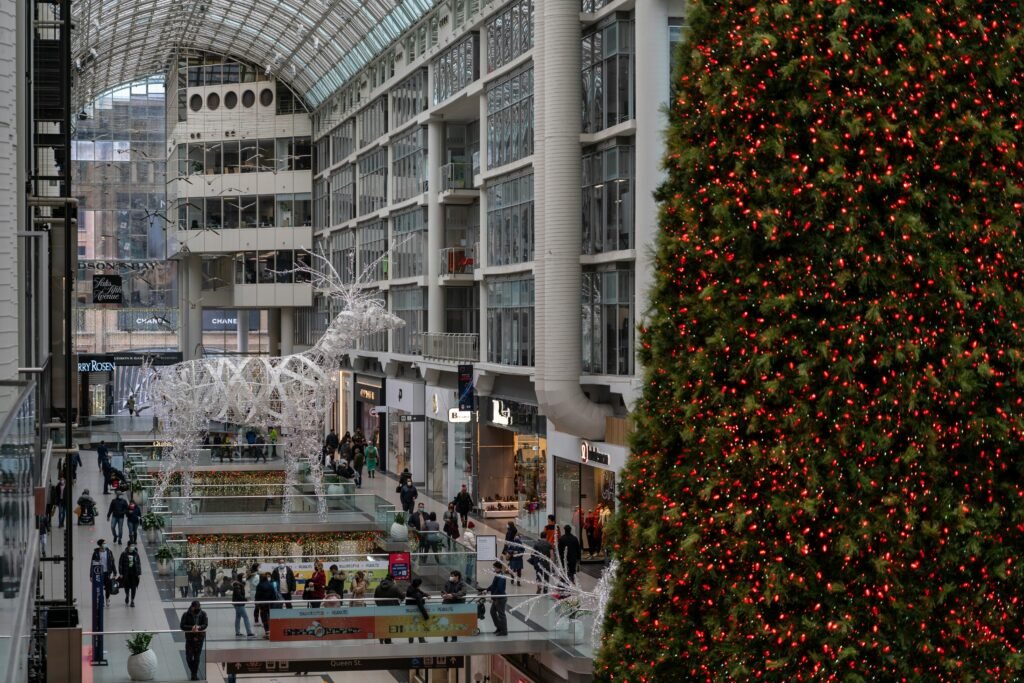 People shopping amidst festive decorations, including a large Christmas tree, inside a Toronto mall.