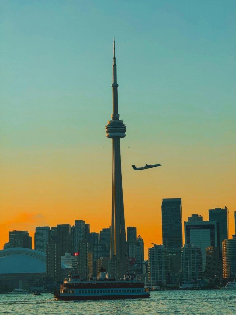 The Toronto skyline featuring the iconic CN Tower during a vibrant autumn sunset, with a plane flying overhead.