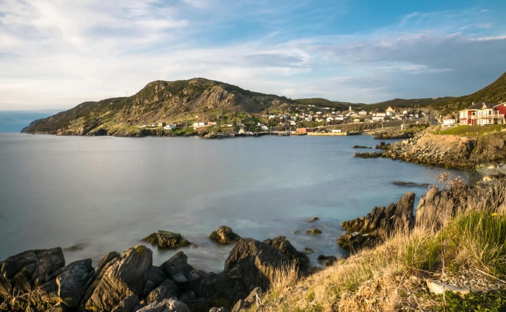 Peaceful coastal landscape with a village by the sea, showcasing rocky shores and scenic mountains.