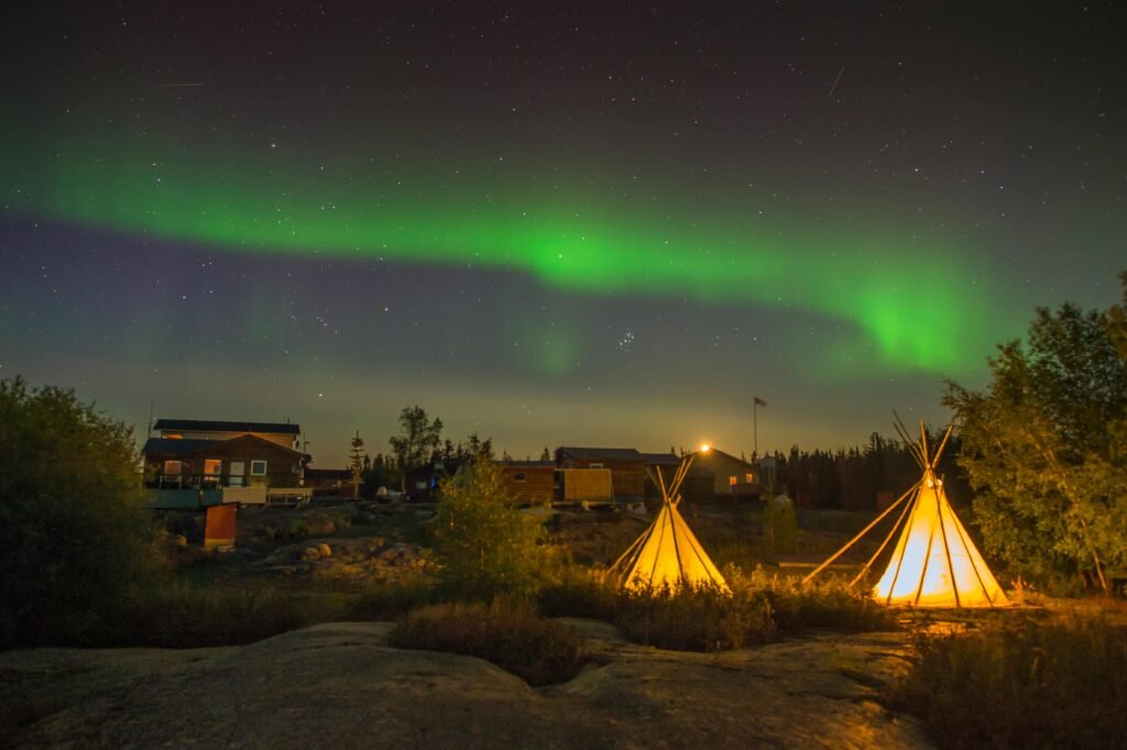 Beautiful Northern Lights illuminating a campsite with tipis in Yellowknife, Canada, at night.